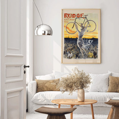 Vintage bicycle poster by Jean de Paleologue showing a triumphant figure and a woman holding a bicycle above a crowd at sunset for Rudge bicycle brand, framed and displayed in home decor
