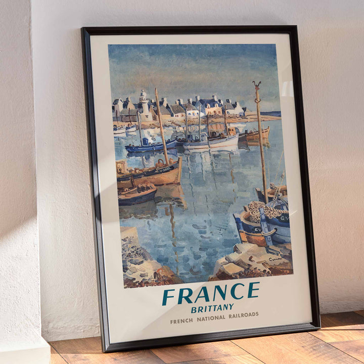 France Brittany Railway poster by Edmond Ceria featuring blue harbor boats, pale village roofs, cream sky, and coastal scenery, framed and displayed in modern living room decor