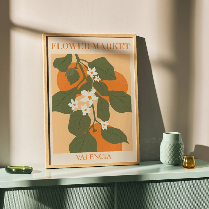 Flower Market Valencia by Moryarty poster illustration with green leaves and white flowers on orange background, framed and displayed in home decor