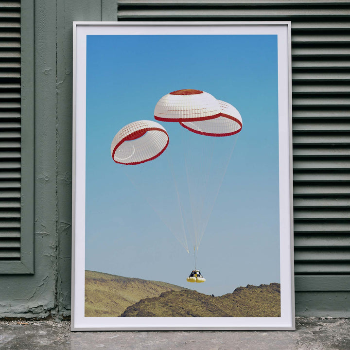 CST-100 crew capsule landing with three parachutes over desert landscape by NASA and The Boeing Company poster artwork, framed and displayed in home decor