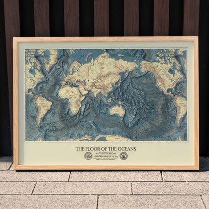World map artwork showing ocean floors titled The Floor of the Oceans bathymetric map poster, framed and displayed in home decor