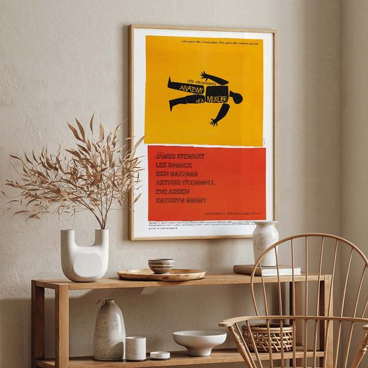 Movie poster of Anatomy of a Murder by Saul Bass features a yellow and red design with a black silhouette of a body, framed and displayed in home decor